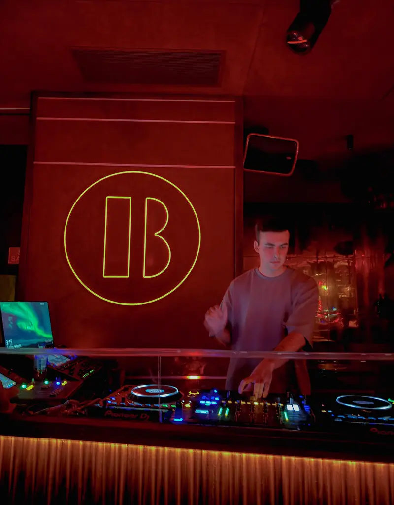 DJ pinchando en una sala de luz roja con un neón circular al fondo