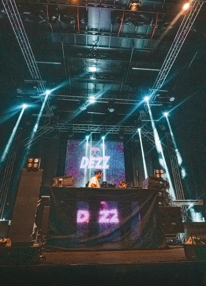 Sala de conciertos con la pantalla del escenario encendida y los focos cruzando el techo